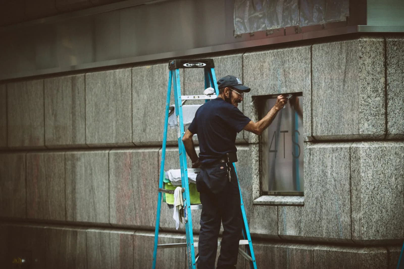 Cleaner in work uniform on a step ladder cleaning a commercial building frontage
